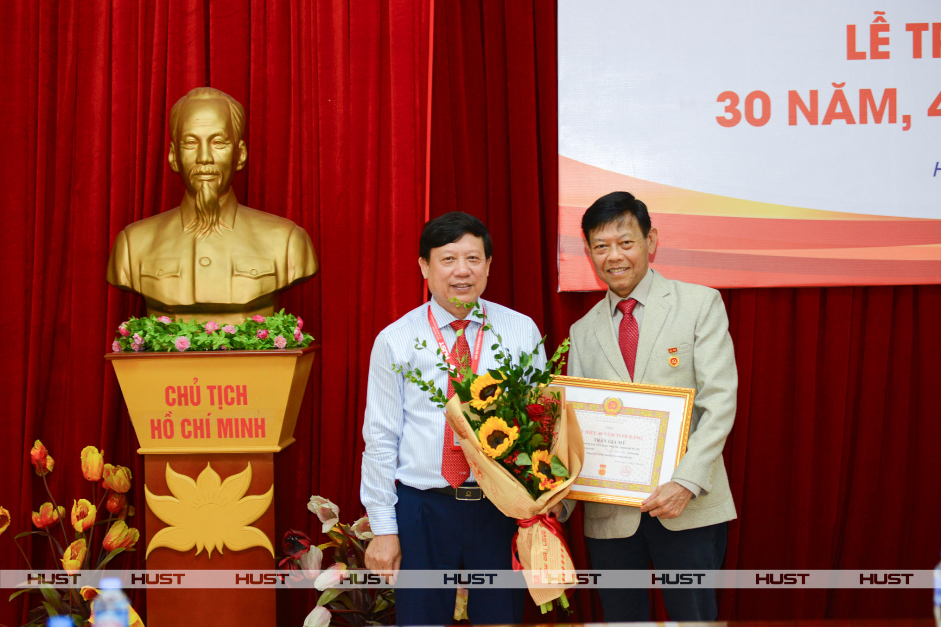 Đồng chí Bùi Đức Hùng - Phó Bí thư Thường trực điều hành Đảng bộ đại học - trân trọng trao Huy hiệu 40 năm tuổi Đảng và tặng hoa chúc mừng đồng chí Trần Gia Mỹ. Ảnh: CCDK